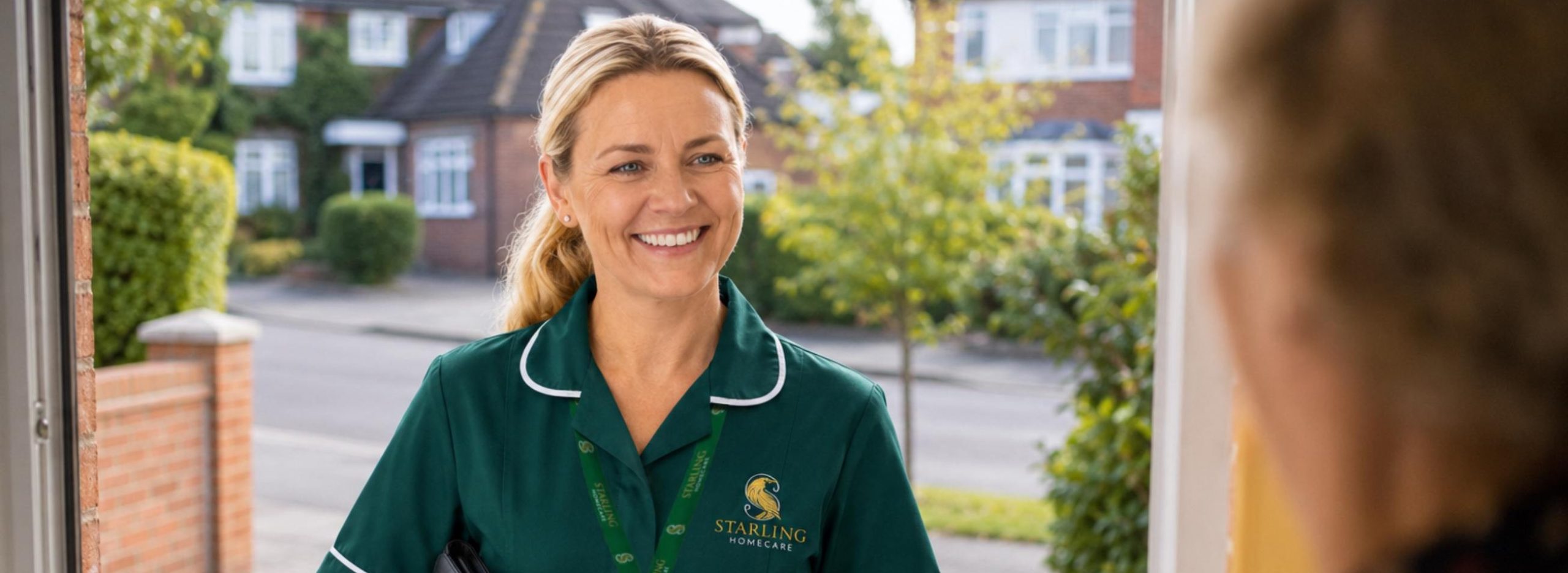 Starling Homecare carer in uniform smiling at a client's front door during a home care visit. Starling Homecare carer in uniform smiling at a client's front door during a home care visit.