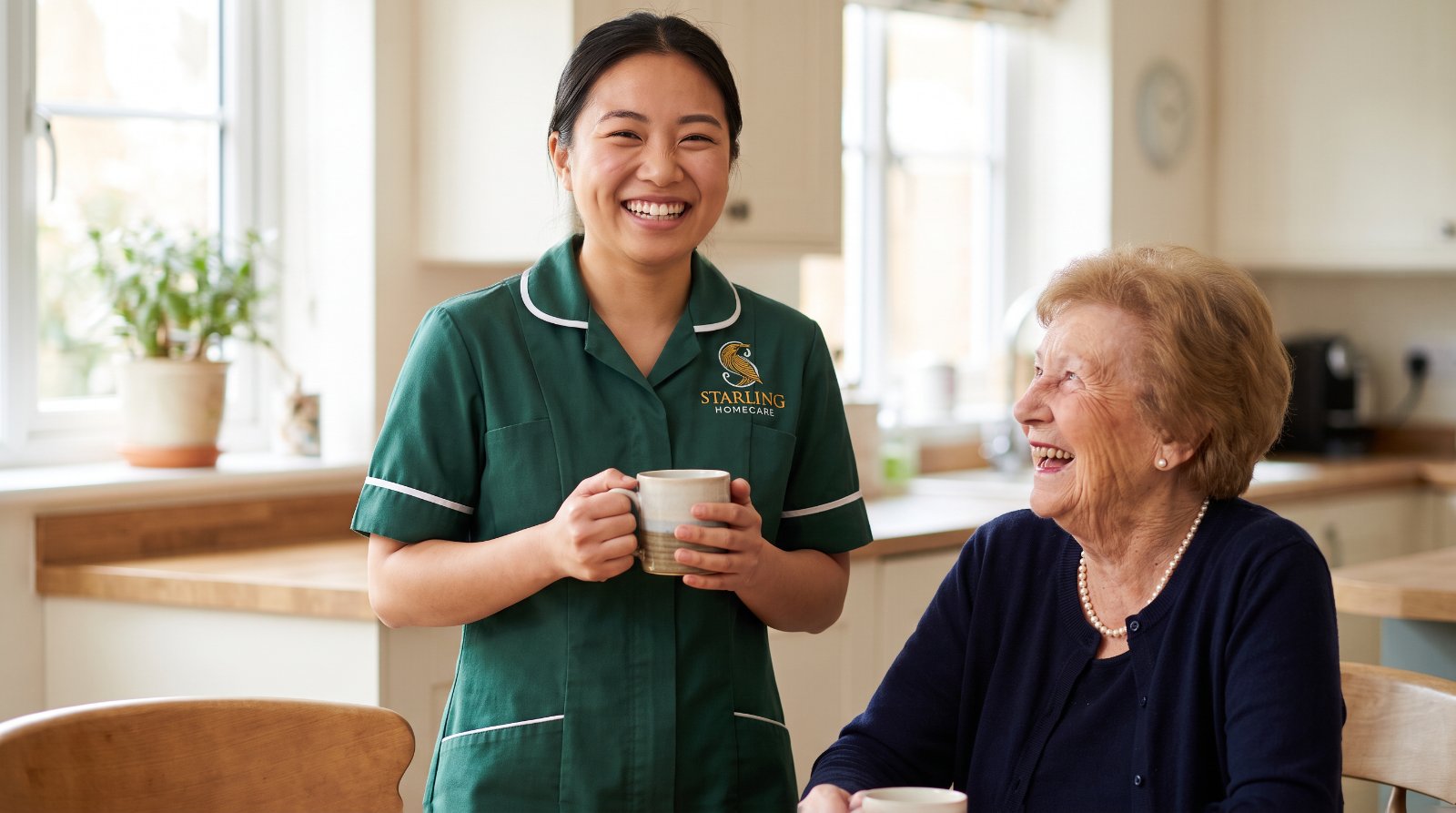 A Starling Homecare carer and an older woman laughing together over a cup of tea in her kitchen while they talk over home care or a care home in St Albans