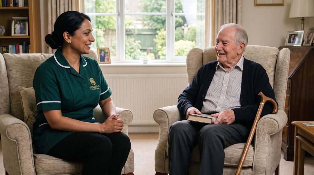 A Starling Homecare carer sitting with an older man in his living room during a later life care visit in Berkhamsted, a walking stick resting beside his chair.