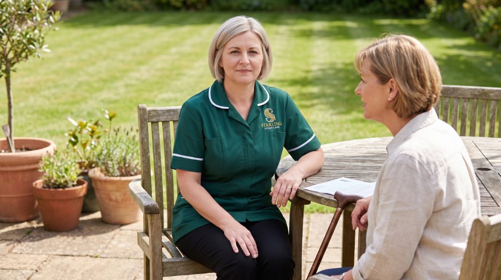 A Starling Homecare carer sitting at a garden table with a woman with MS, her walking stick beside her, talking through MS support in Hertfordshire