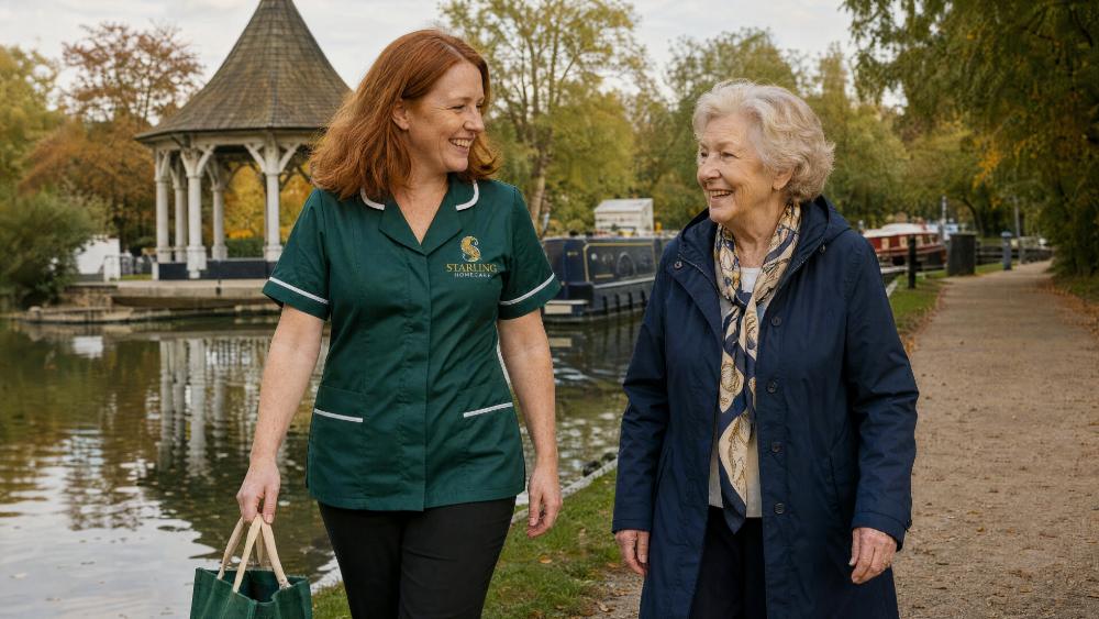 Companionship Care in Ware and Hoddesdon: What to Expect Carer in a bottle green uniform walking by the river with an older woman, companionship care in Ware and Hoddesdon